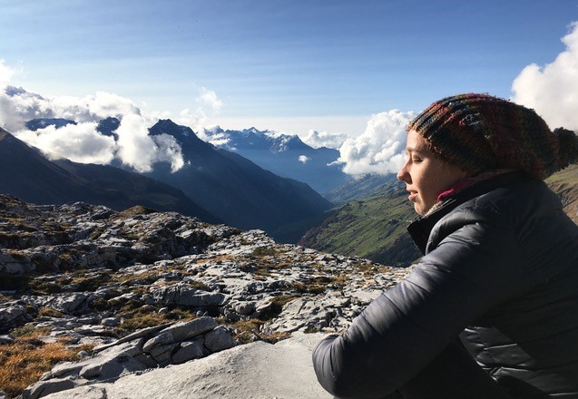 picture of a person sitting in the mountains with her eyes closed and the clouds floating beneath