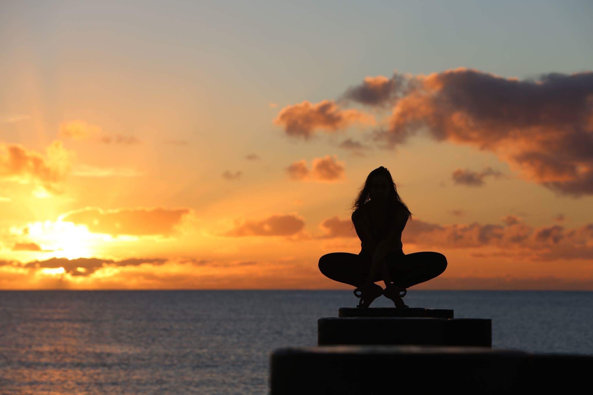 a woman with her back to the camera holding a yoga pose during a beautiful sunset