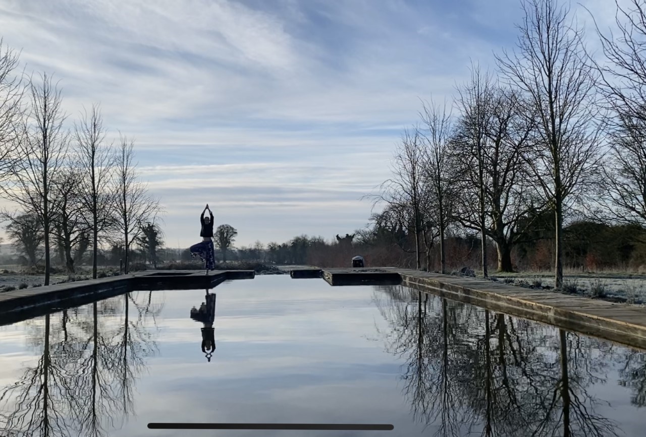 a person holding the tree pose reflected across a lake